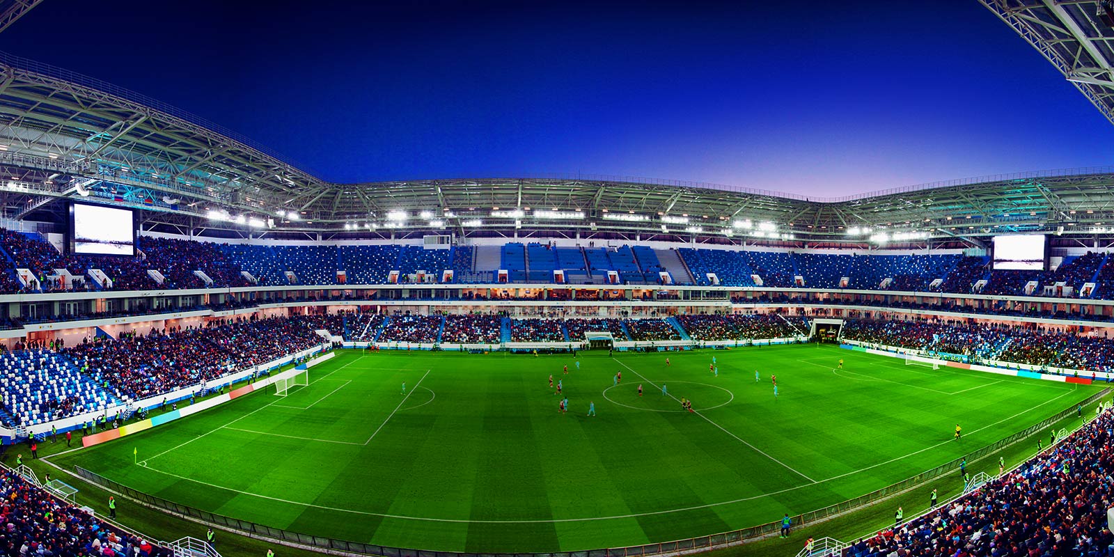 A wide-angled view of a football stadium with a full crowd and match in progress.