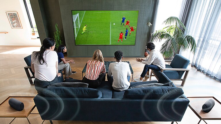 5 people gathered in front of a wall mounted flatscreen TV watching a football game.