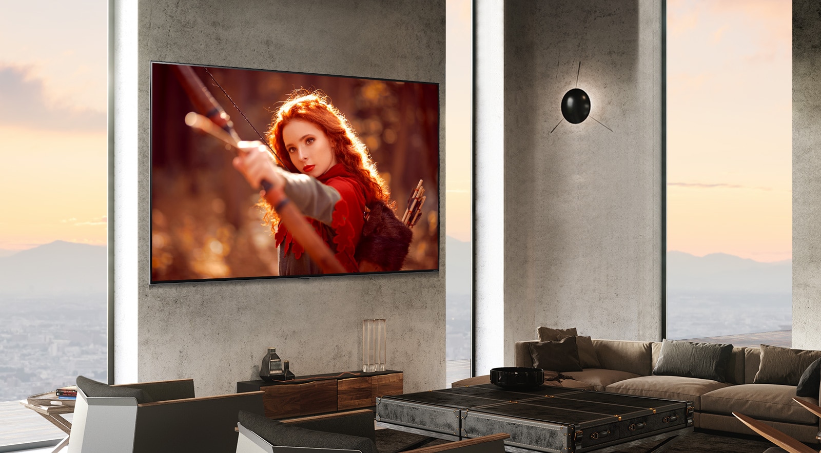 A large TV mounted against a grey stone wall next to floor-to-ceiling windows in a modern room. The screen shows a red-haired woman holding a bow pointed towards the camera.