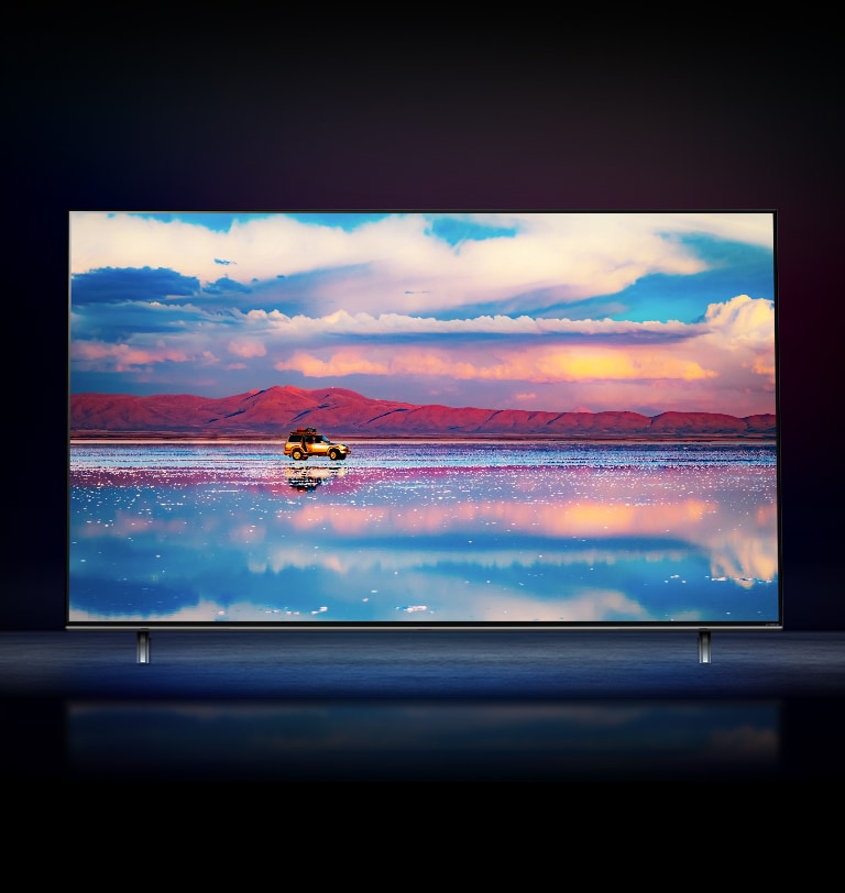 An LG NanoCell TV against a black background. The TV shows a car driving in front of a low mountain range in water that reflects the vivid sky.