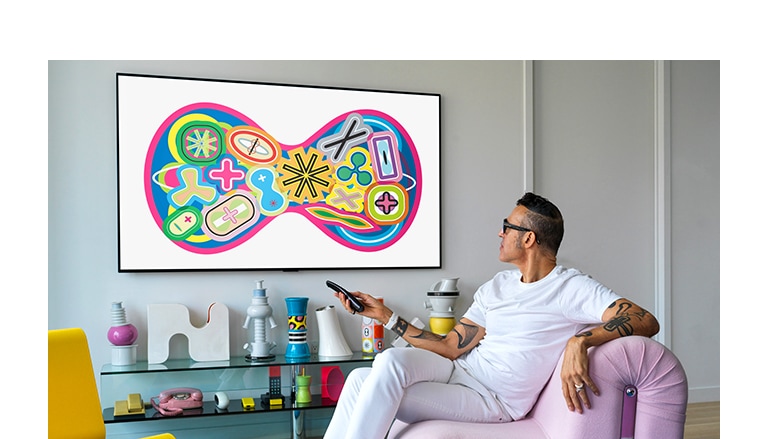 An industrial designer, Karim Rashid sitting on a sofa is watching a TV displaying a painting. 