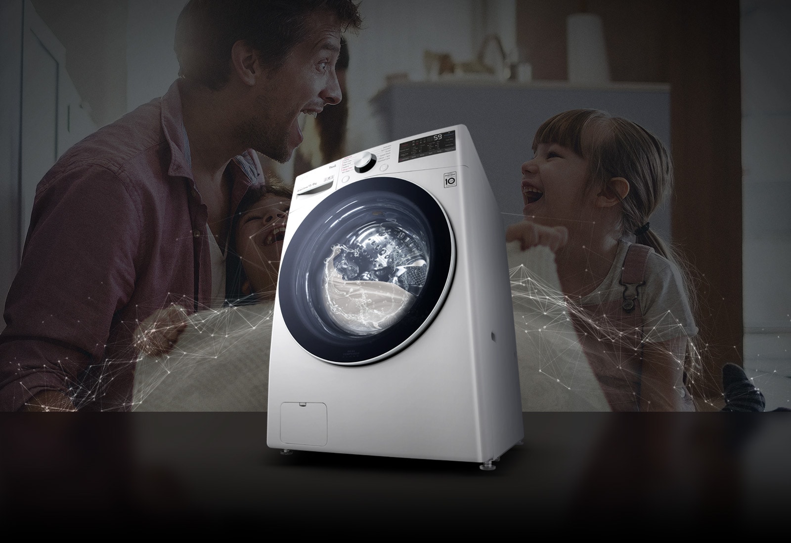 Father and daughters laugh in the background as they hold a clean blanket. A White washing machine front load washer in the foreground.