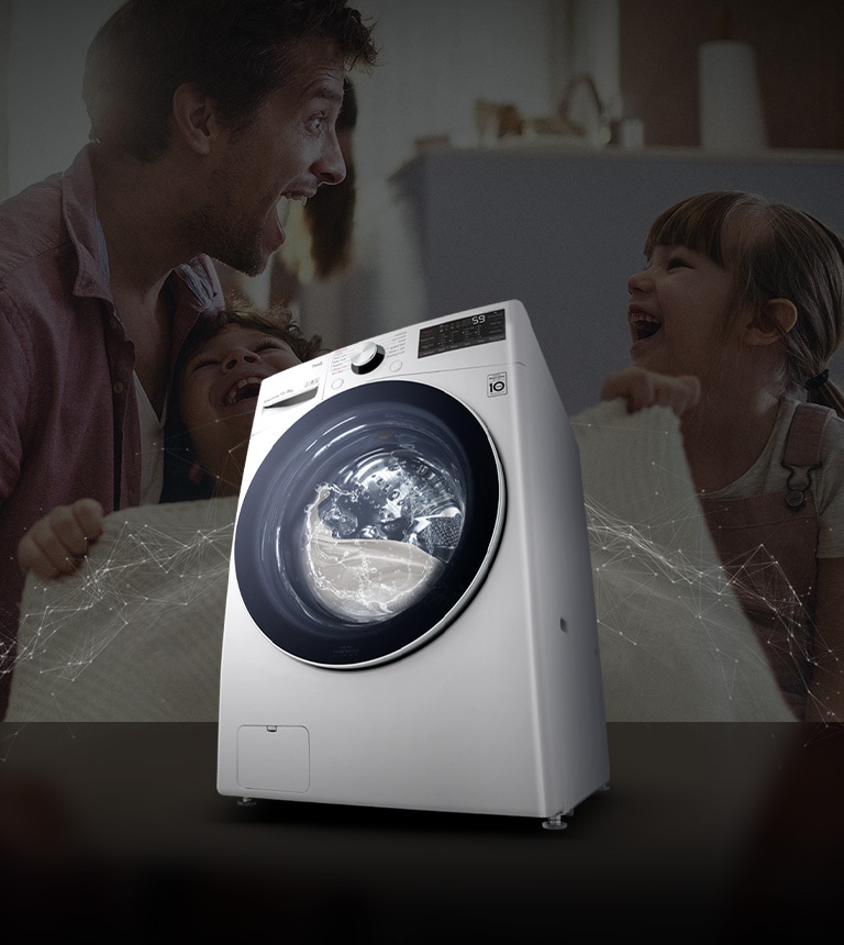 Father and daughters laugh in the background as they hold a clean blanket. A White washing machine front load washer in the foreground.